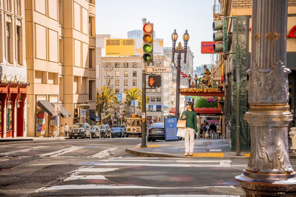 A young woman standing at a San Francisco city street corner with a stoplight and buildings surrounding her